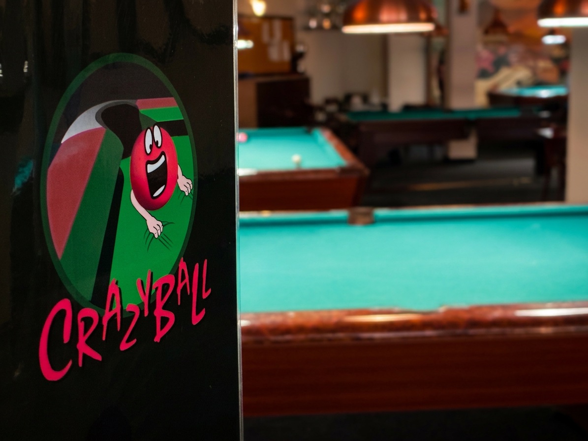 Crazyball-Logo an einer Säule, dahinter die Billardtische