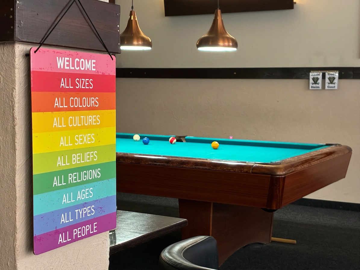 Welcome-Schild in Regenbogenfarben neben einem Billardtisch